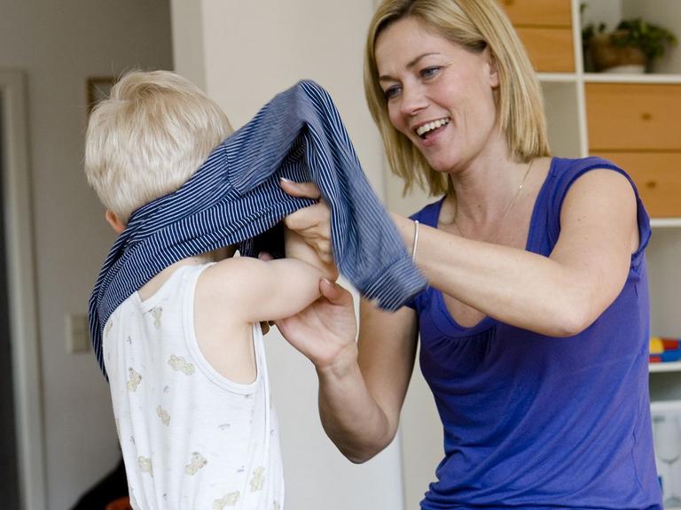 kvinde hjælper et barn med at tage trøje på